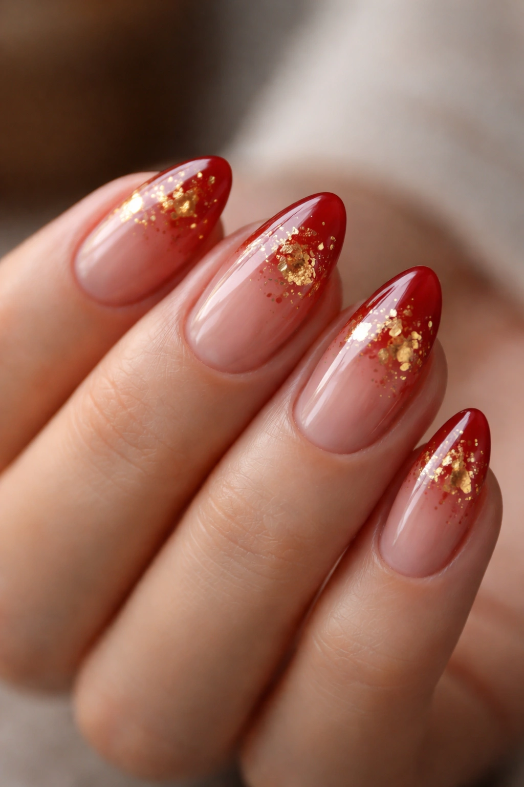 Close-up of short almond nails with sheer red and gold leaf accents