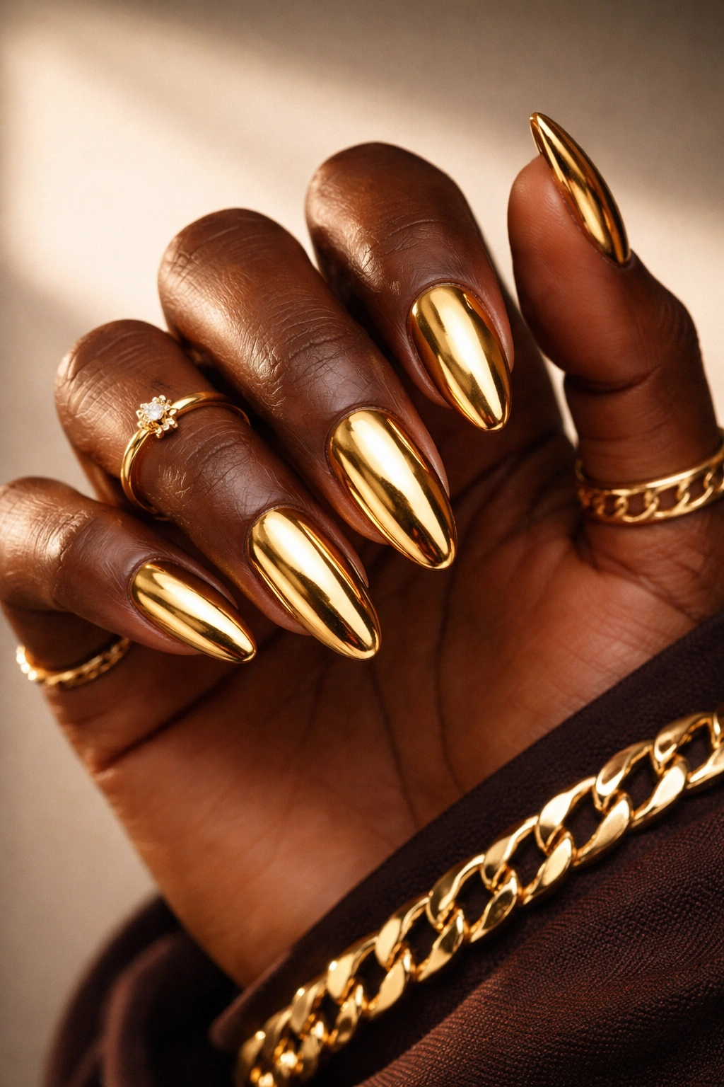 Close-up of dark-skinned hand with glossy gold nails on a neutral background