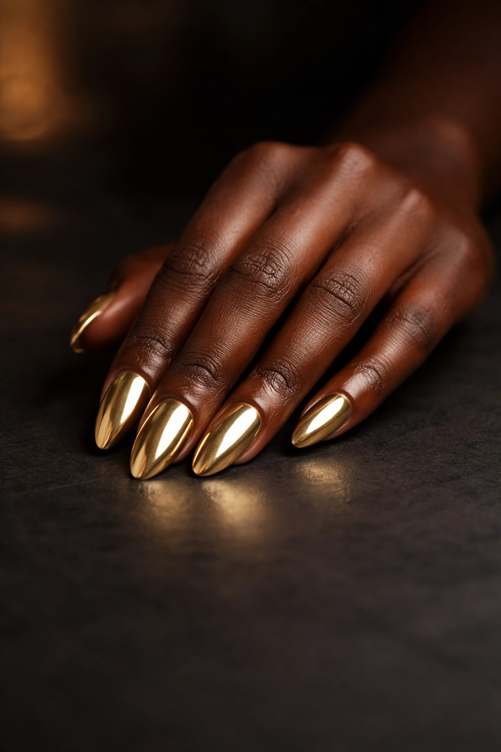 Close-up of dark-skinned hand with gold nails on dark matte surface