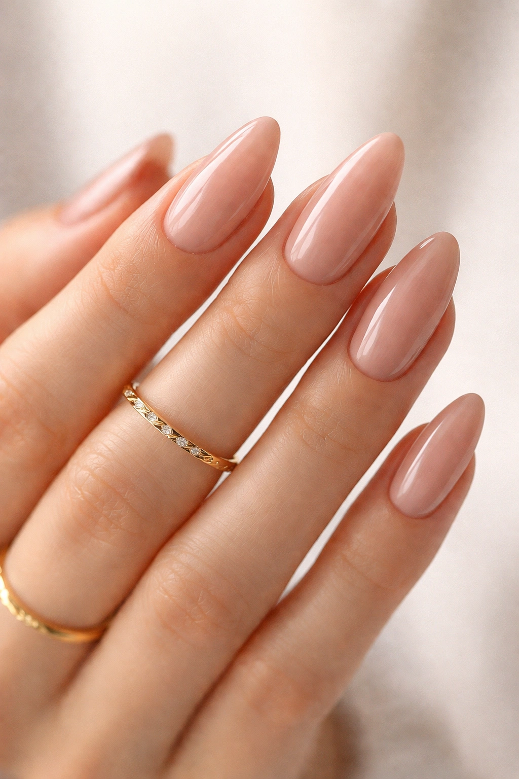 Close-up of almond nails with soft pink nude polish and a delicate gold ring