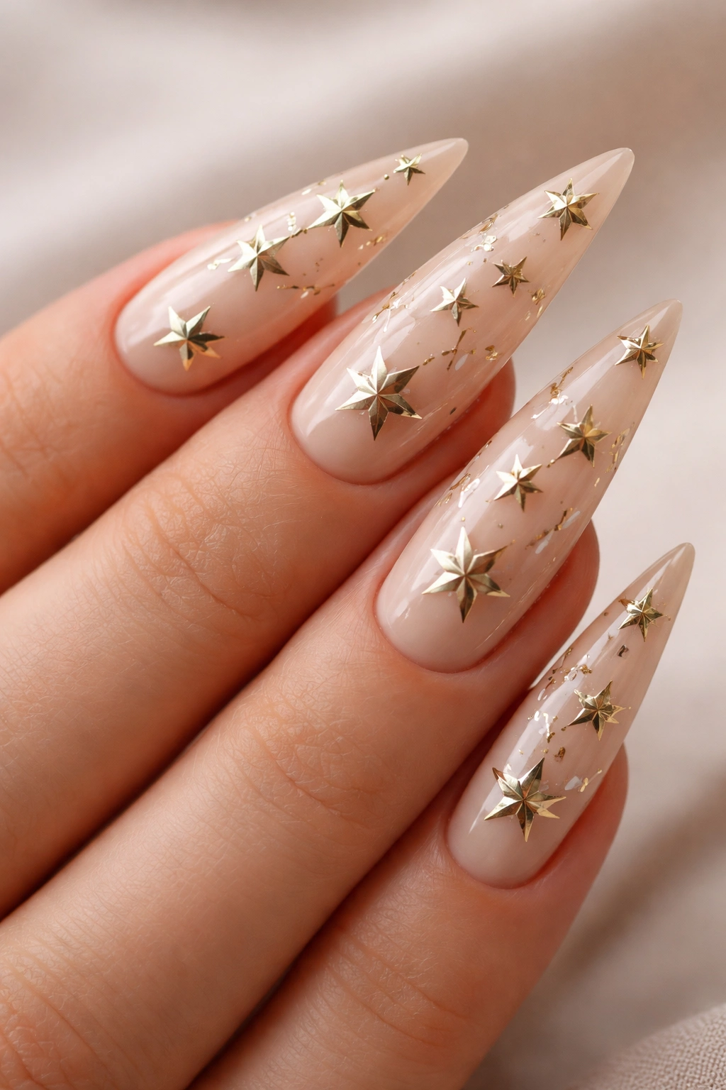 Gold star accents on nude stiletto nail with constellation layout