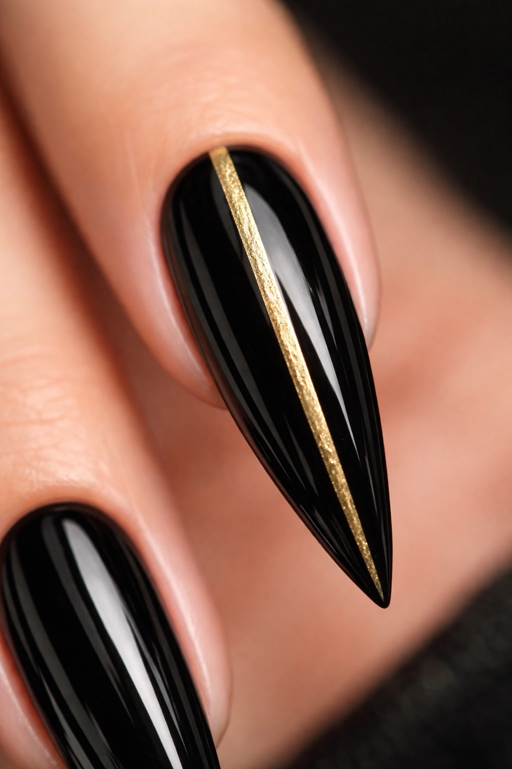 Close-up of a glossy black stiletto nail with a gold vertical stripe