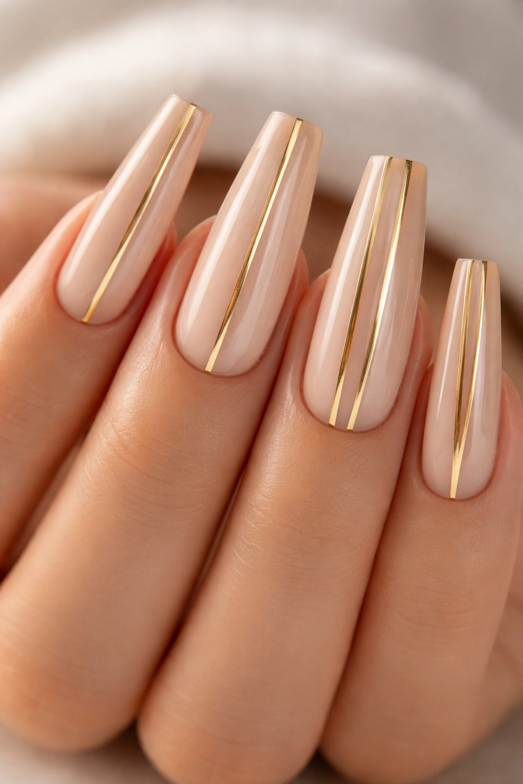 Close-up of long coffin nails with gold striped lines on nude base