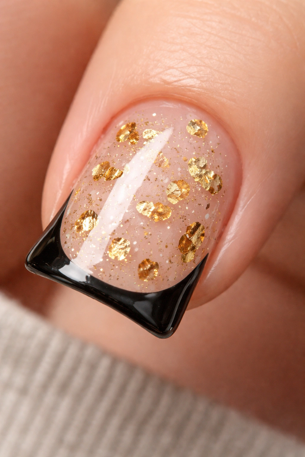 Close-up of a clear-base nail with gold foil flakes and a black outline around the curved duck tip.