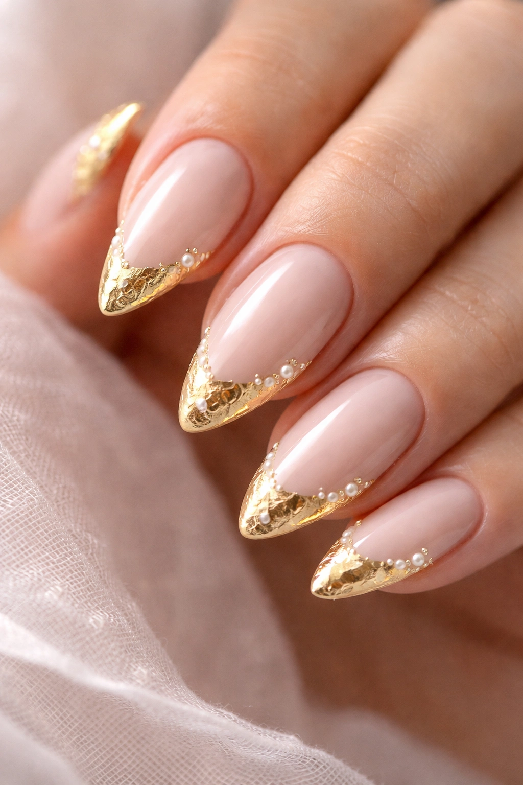 Almond nails with pale nude base, gold foil tips and pearl accents