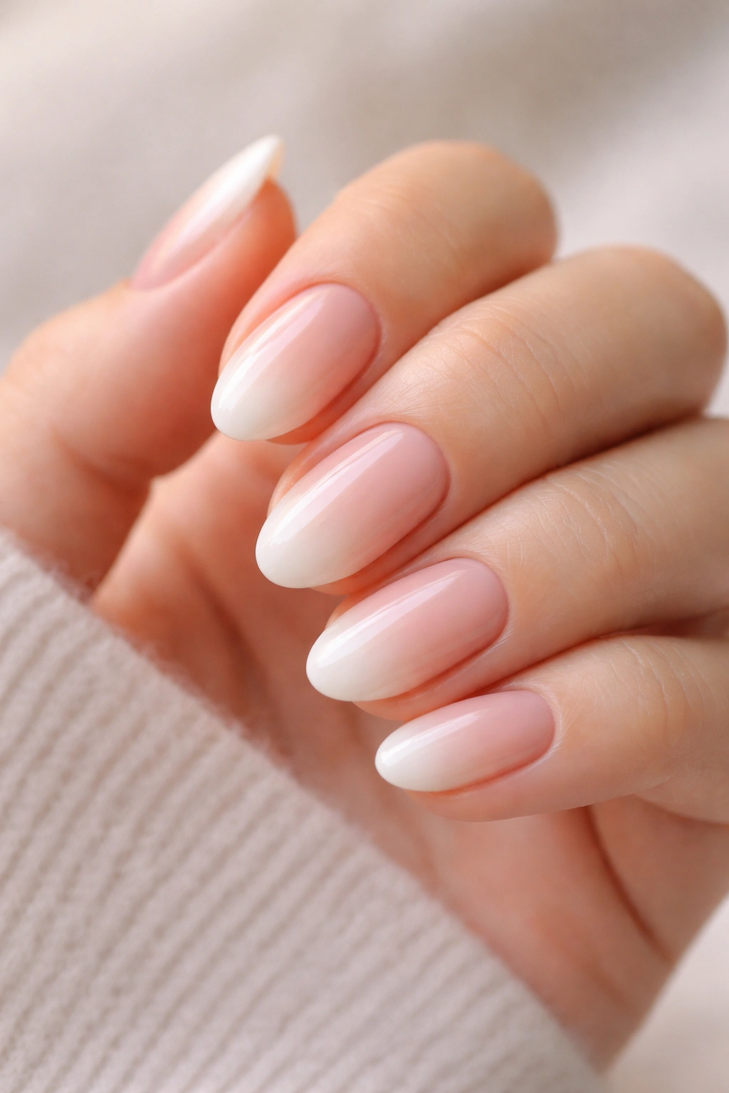 Close-up of short almond nails with a soft gradient French tip on a neutral background