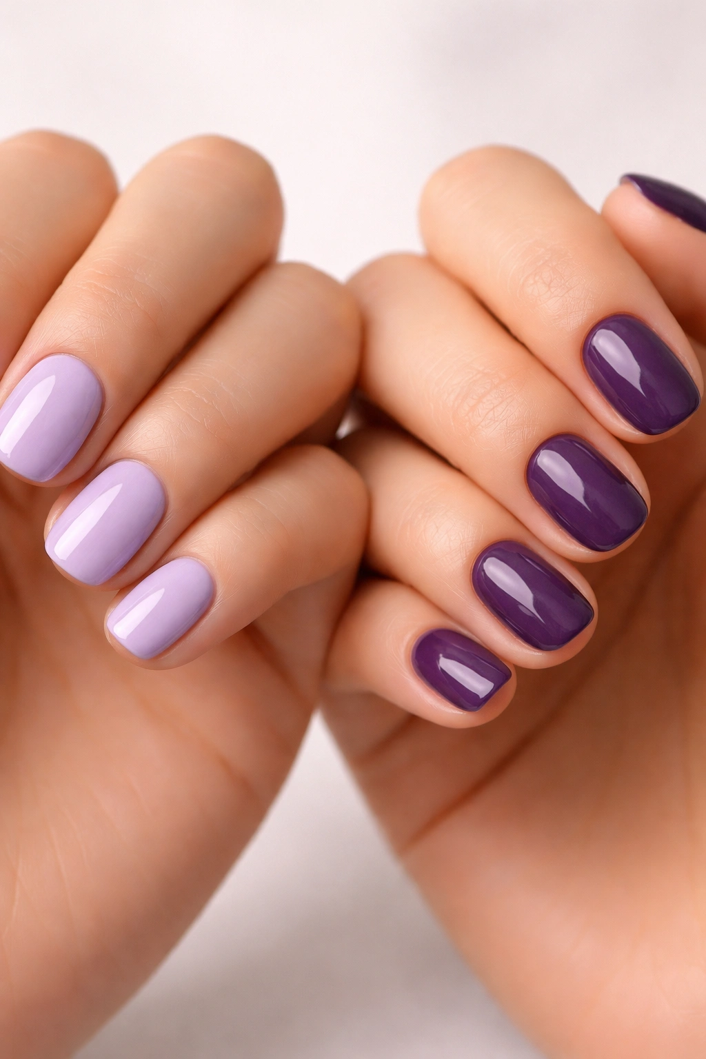 Two hands with short nails in gradient lavender to purple demonstrating different shades.