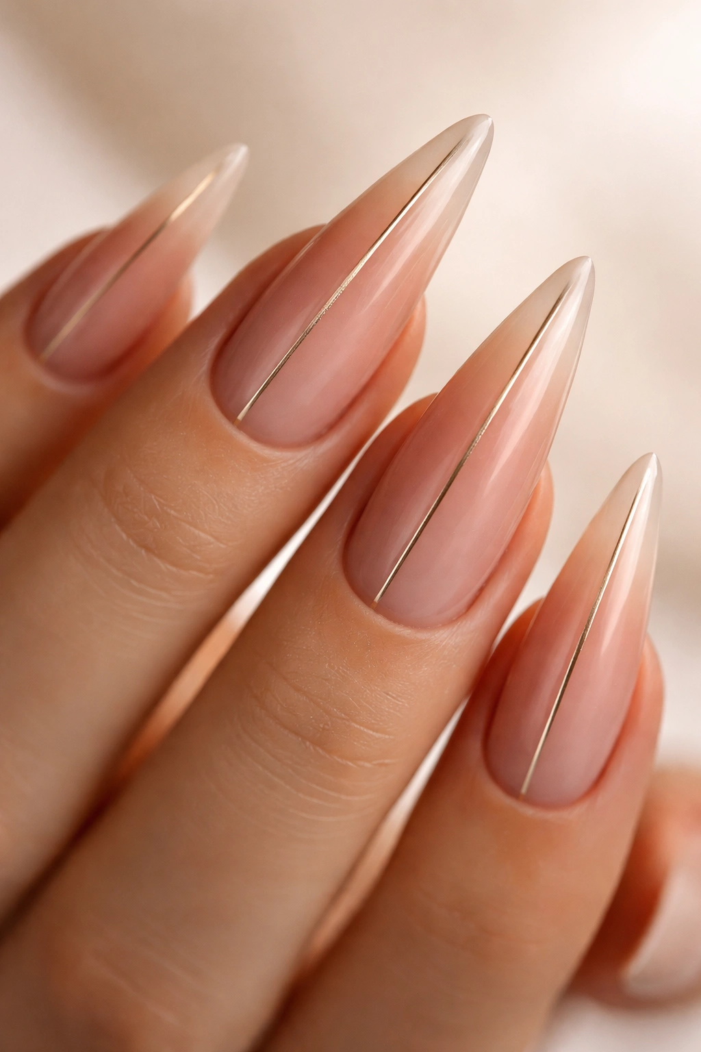 Close-up of nude gradient gel stiletto nails with a fine metallic line