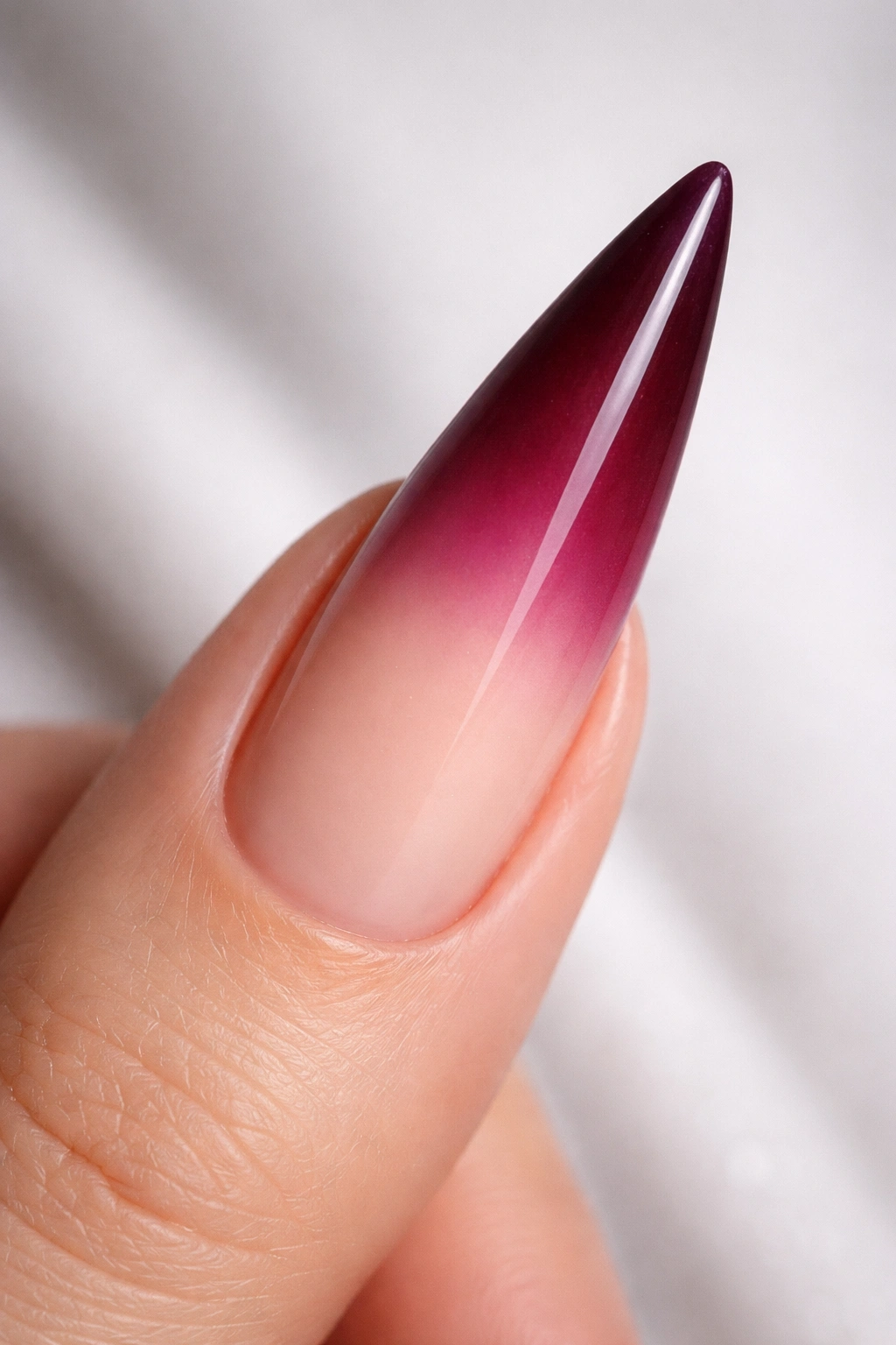 Close-up of a stiletto nail with burgundy to nude ombré gradient, seamless transition