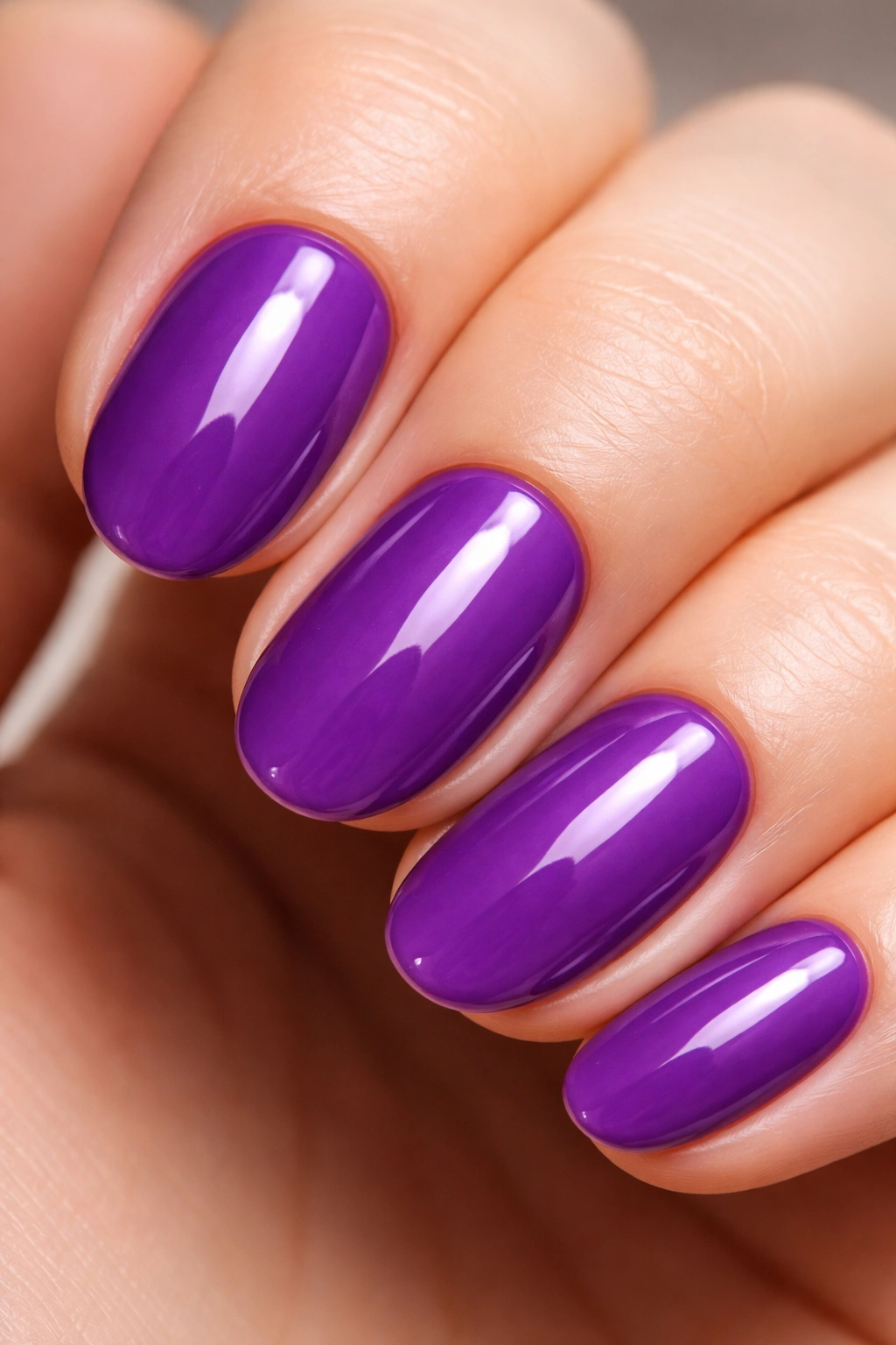 Close-up of a grape purple short oval nail with glossy finish on pale background