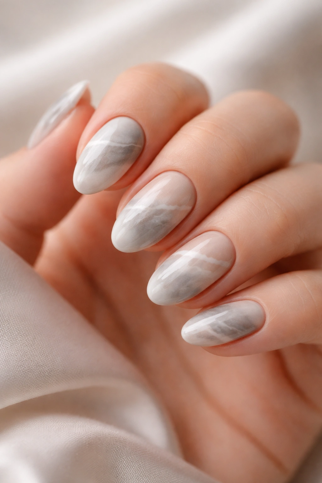 Close-up of short almond nails with gray and nude marble in a satin finish