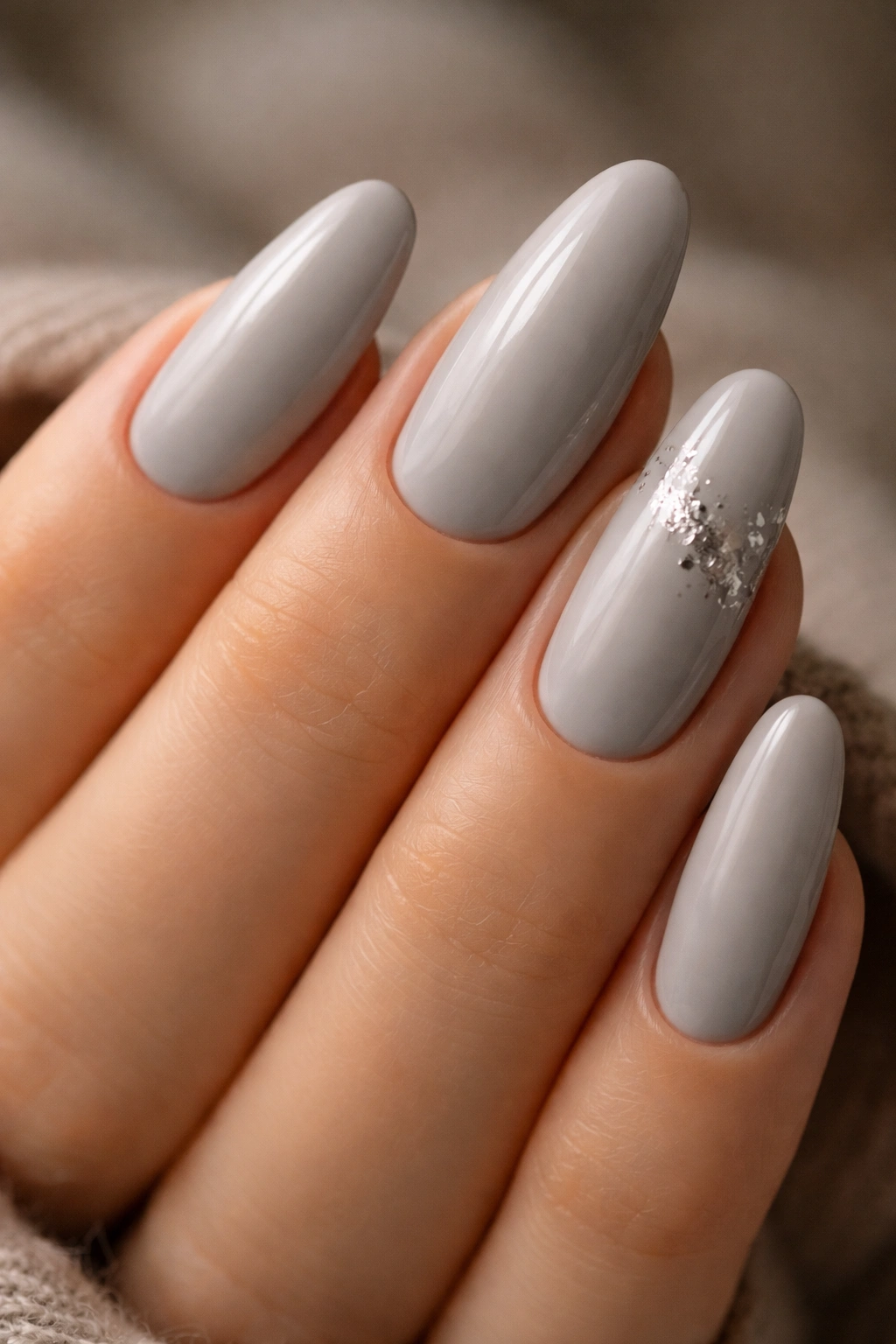 Close-up of long oval nails in soft gray cashmere with a silver accent
