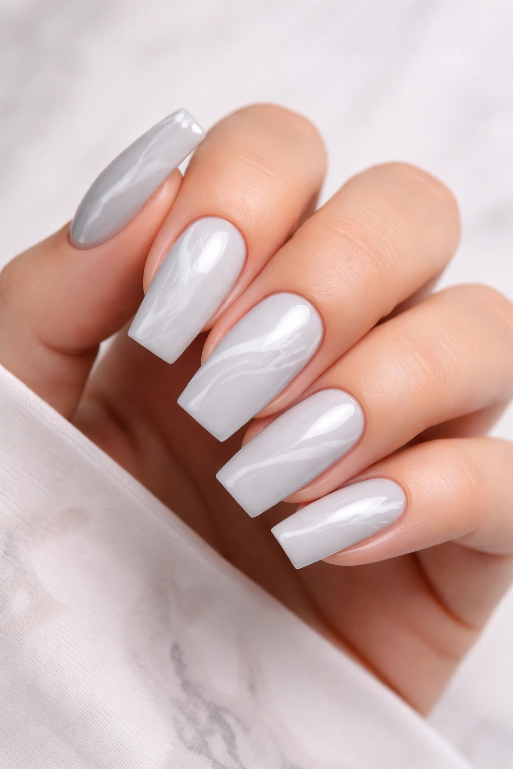 Close-up of soft gray nails with white marble veining on a neutral background