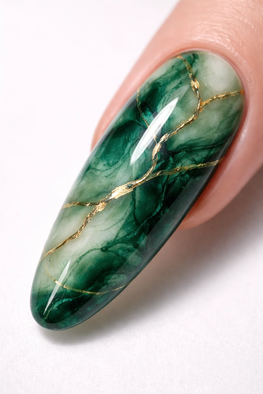 Close-up of a long oval nail with green marble and gold veining