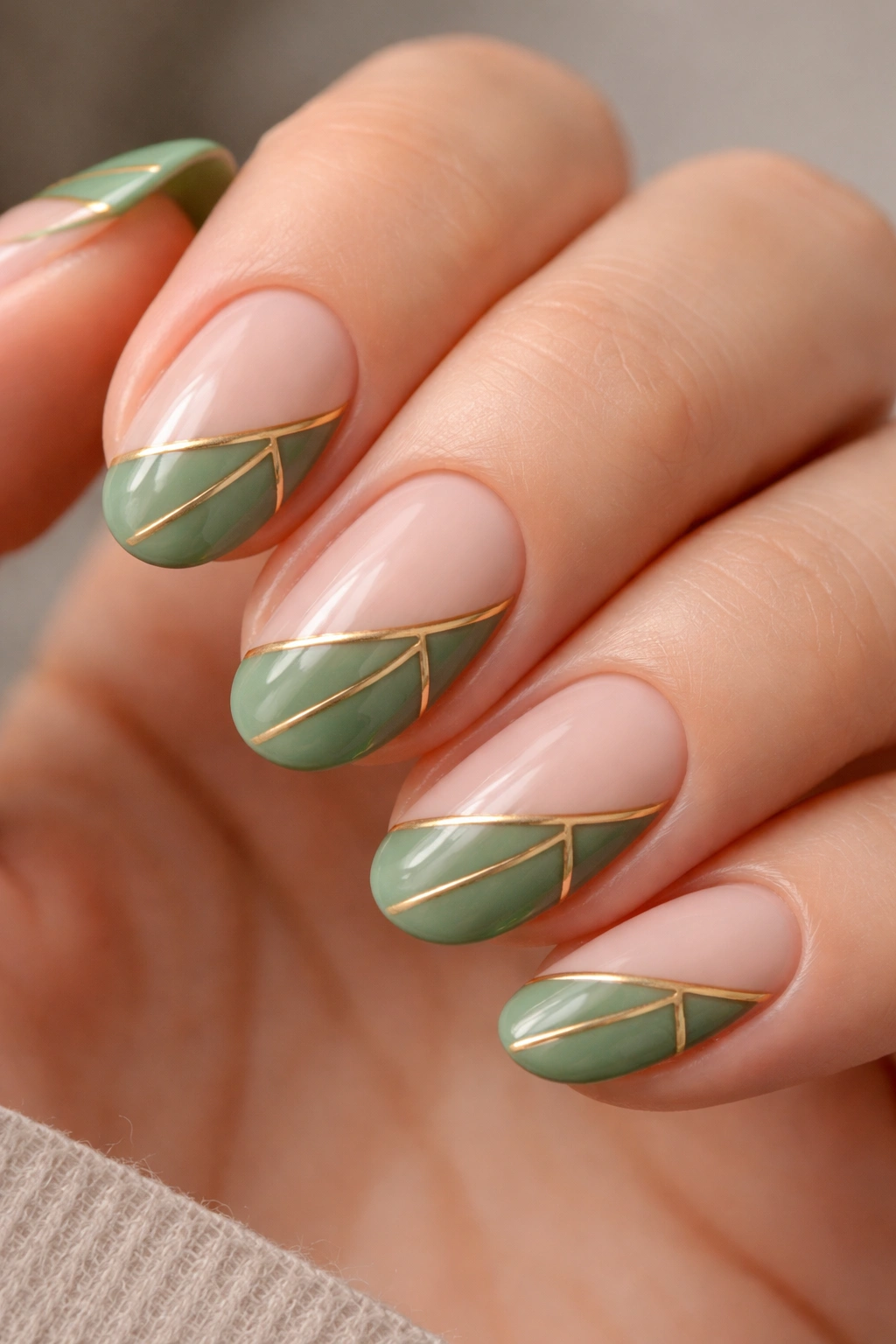 Close-up of short almond nails with green tips featuring gold geometric lines