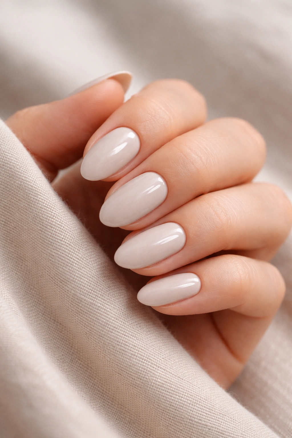 Glossy greige cream short almond nails on a clean hand backdrop