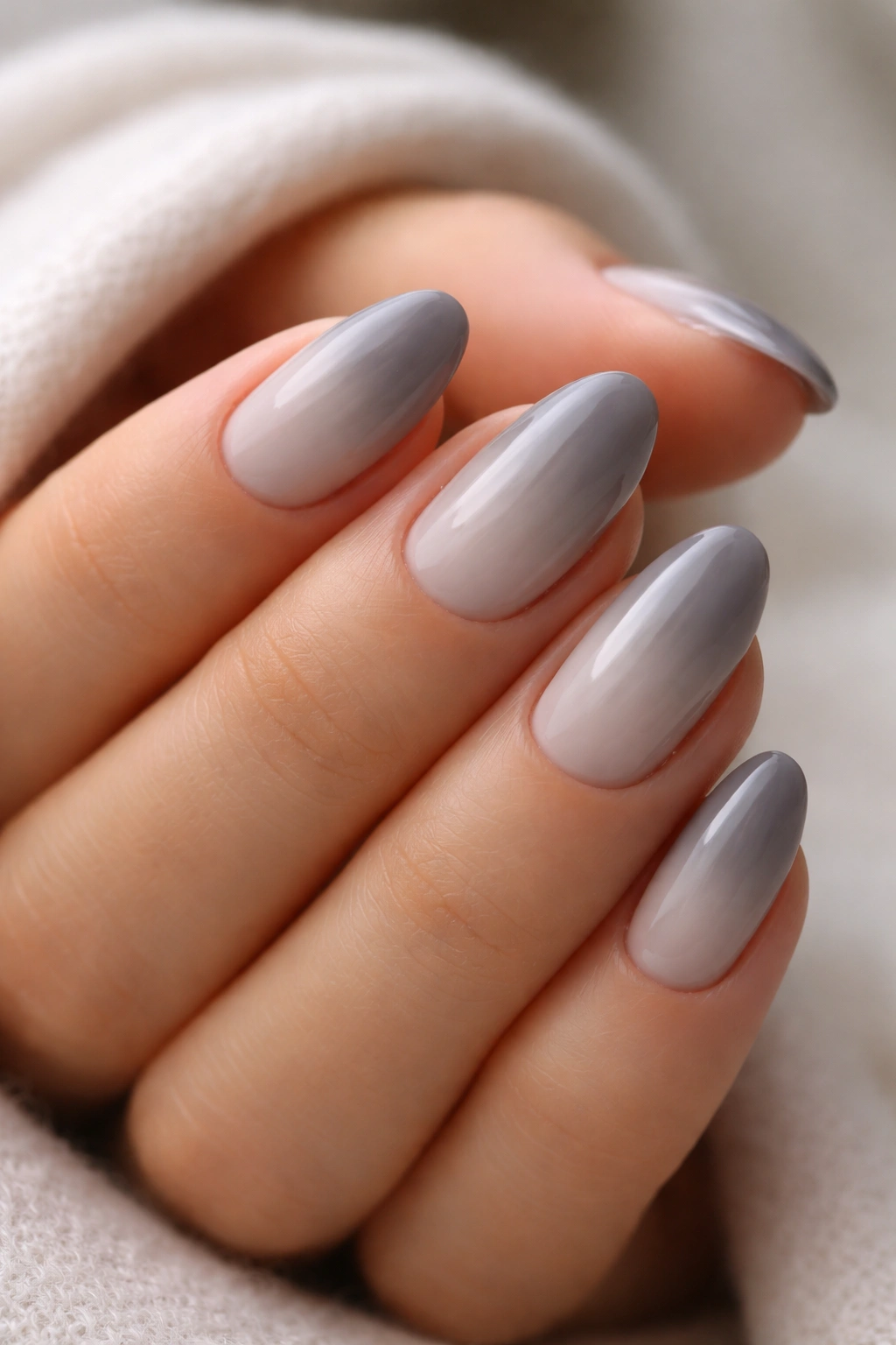 Close-up of short almond nails with pale dove grey base fading to darker tip