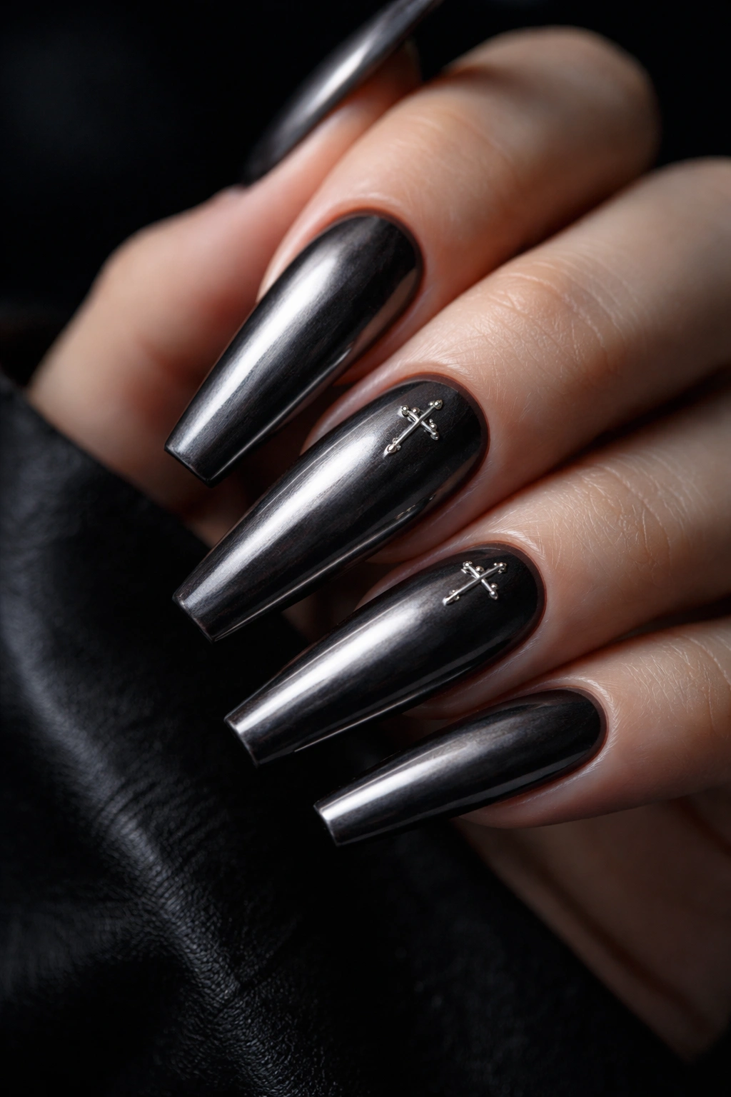Close-up of gunmetal chrome ballerina nails with tiny silver cross accents on a dark background