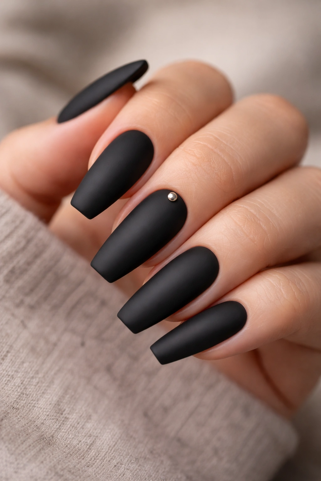 Matte black nail with a single gunmetal stud near the cuticle