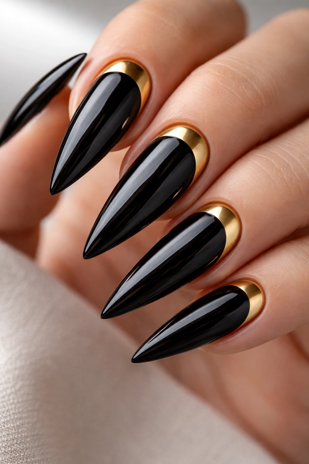 Black stiletto nail with a half-moon gold accent at the cuticle