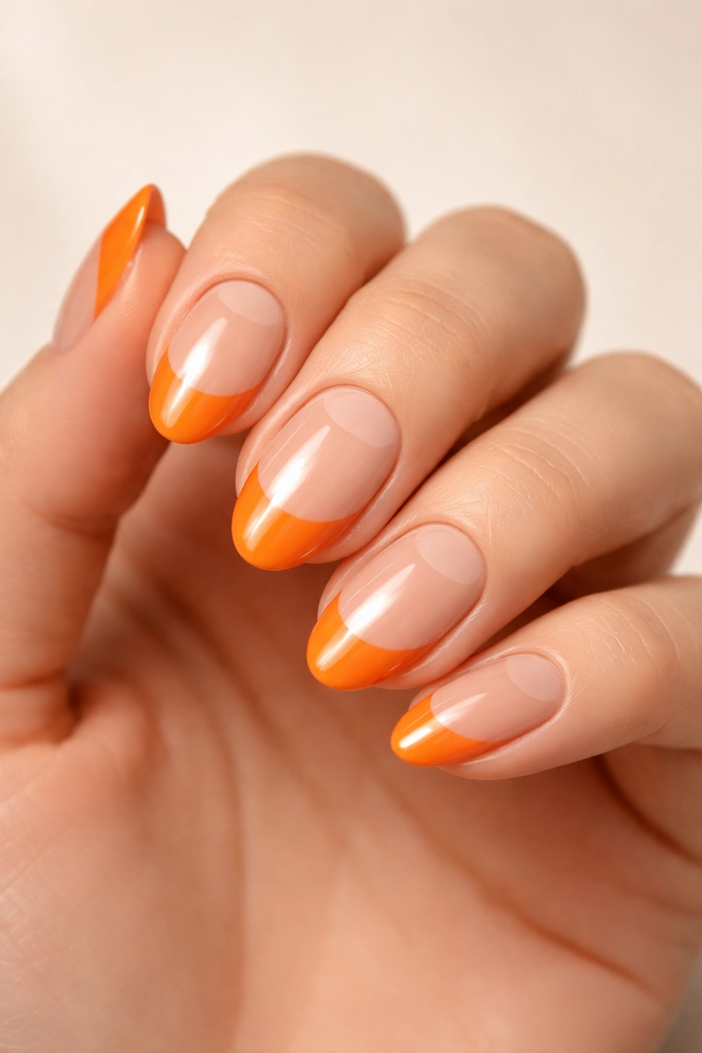 Close-up of half-moon orange nails with nude base