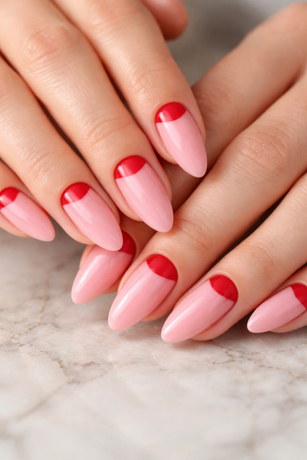 Close-up of almond nails with pink base and red half-moon near cuticle, glossy finish