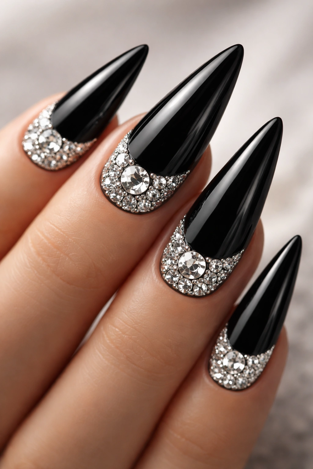 Black stiletto nail with rhinestone-filled half-moon accent at base