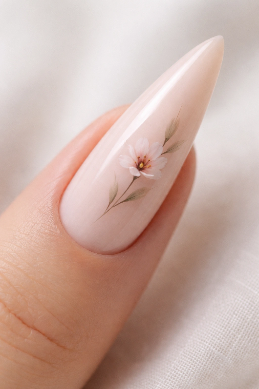 Close-up of a nude stiletto nail with a small hand-painted flower