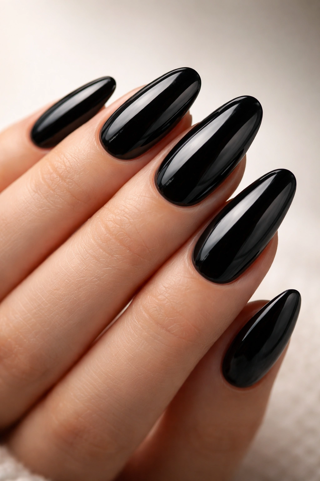 Close-up of long oval nails with high-gloss jet-black polish on a bare hand