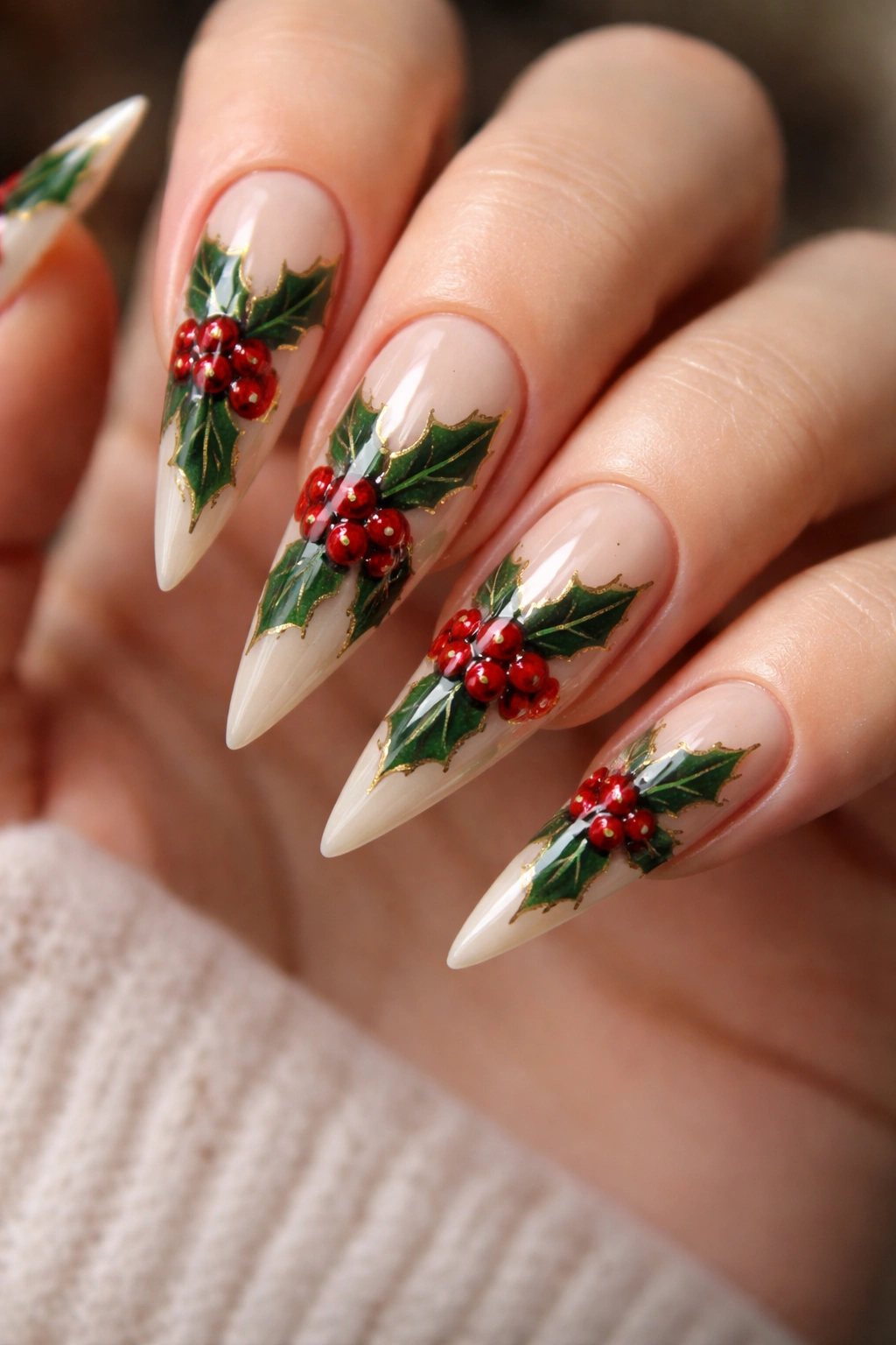 Close-up of holly-inspired stiletto nails with nude base, green leaves and red berries