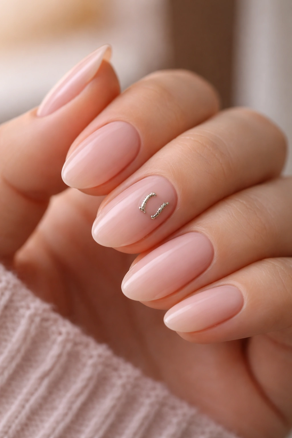 Close-up of nails with a tiny metallic horseshoe accent on pale pink base