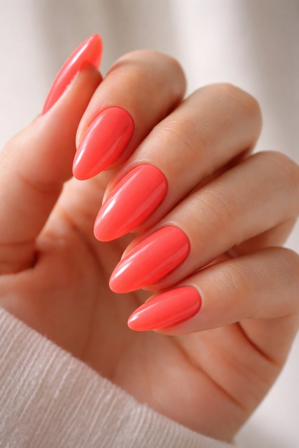 Close-up of hot coral almond nails with glossy finish on a hand