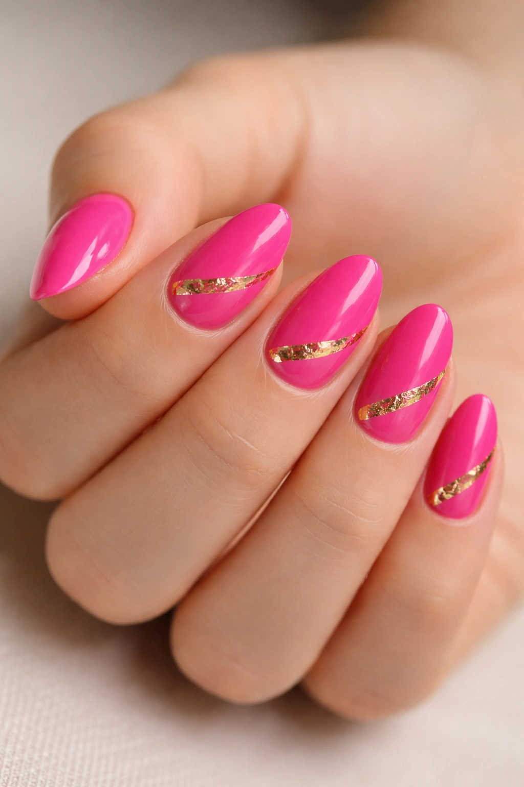 Close-up of short almond nails in hot pink with gold foil accents