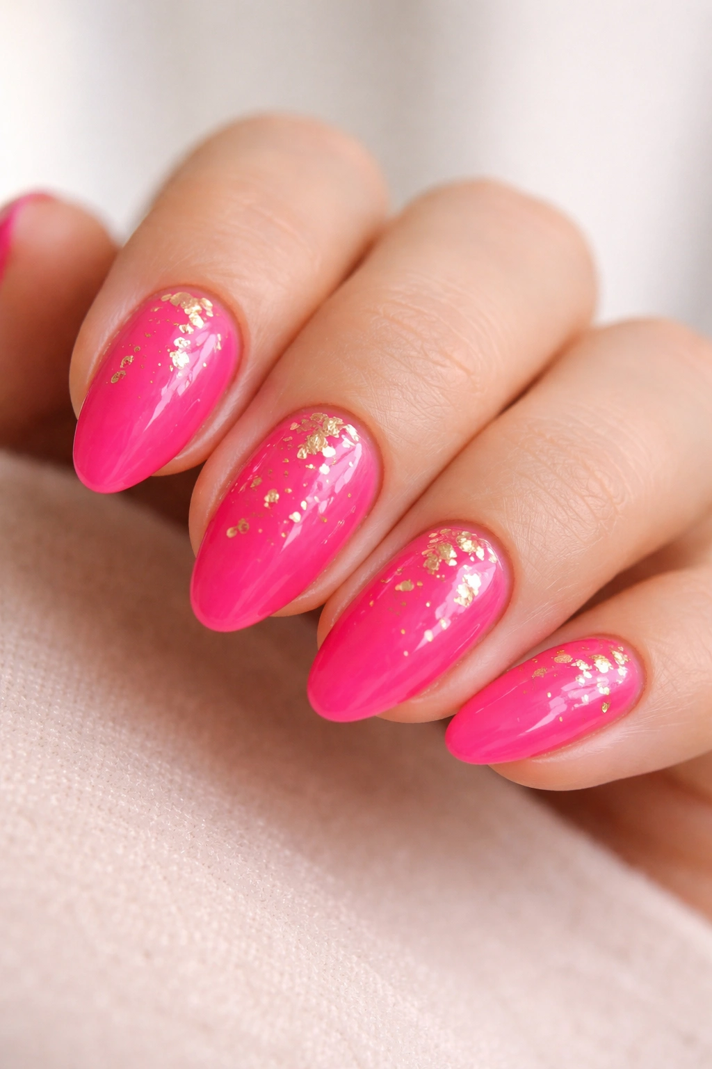 Short hot pink almond nails with scattered gold foil accents
