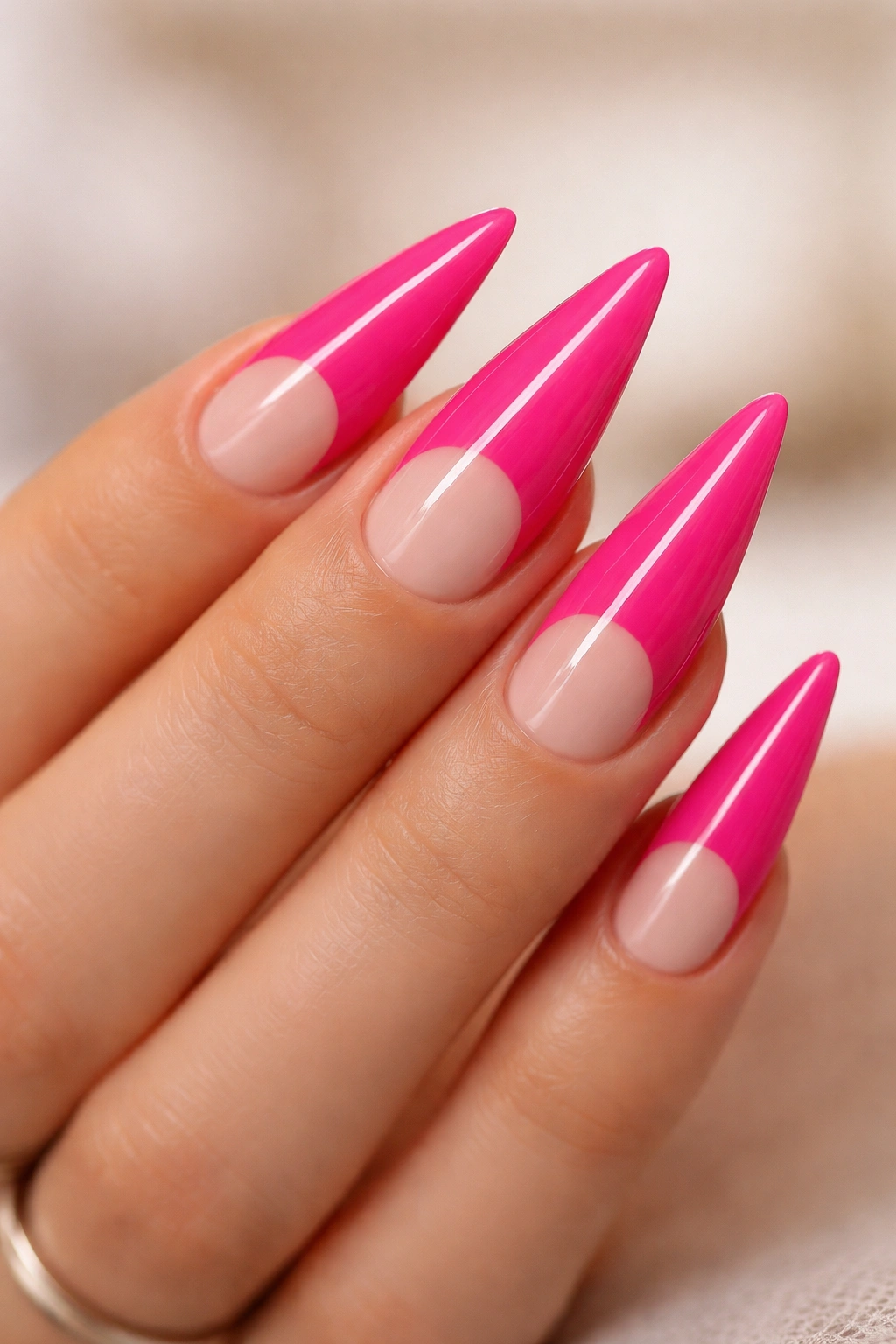 Close-up of hot pink stiletto nails with nude half-moon base design, glossy finish.