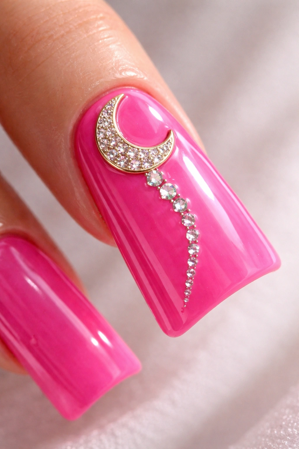 Close-up of a hot pink nail with moon charm and rhinestone trail