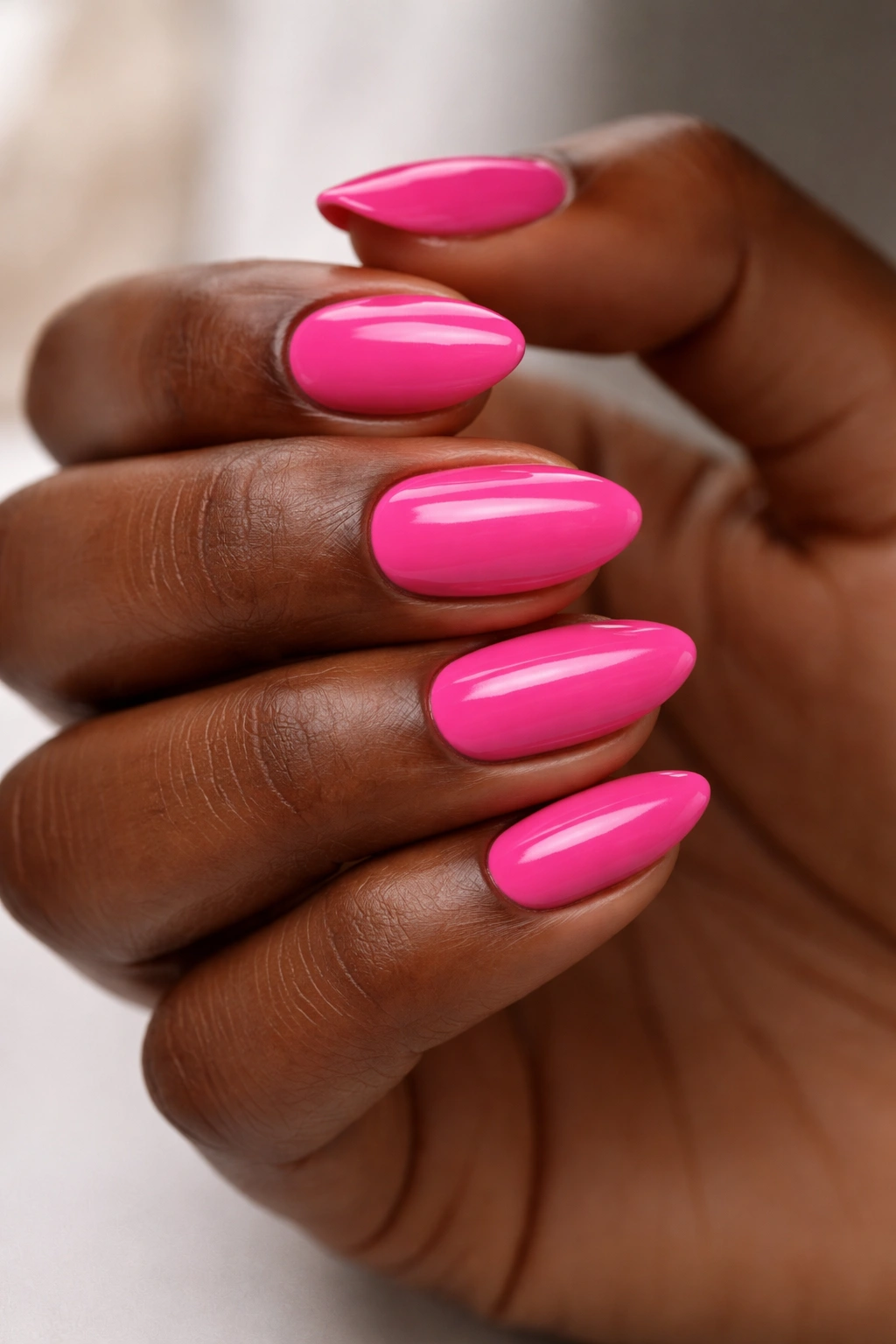 Close-up of hot pink short almond nails on dark skin