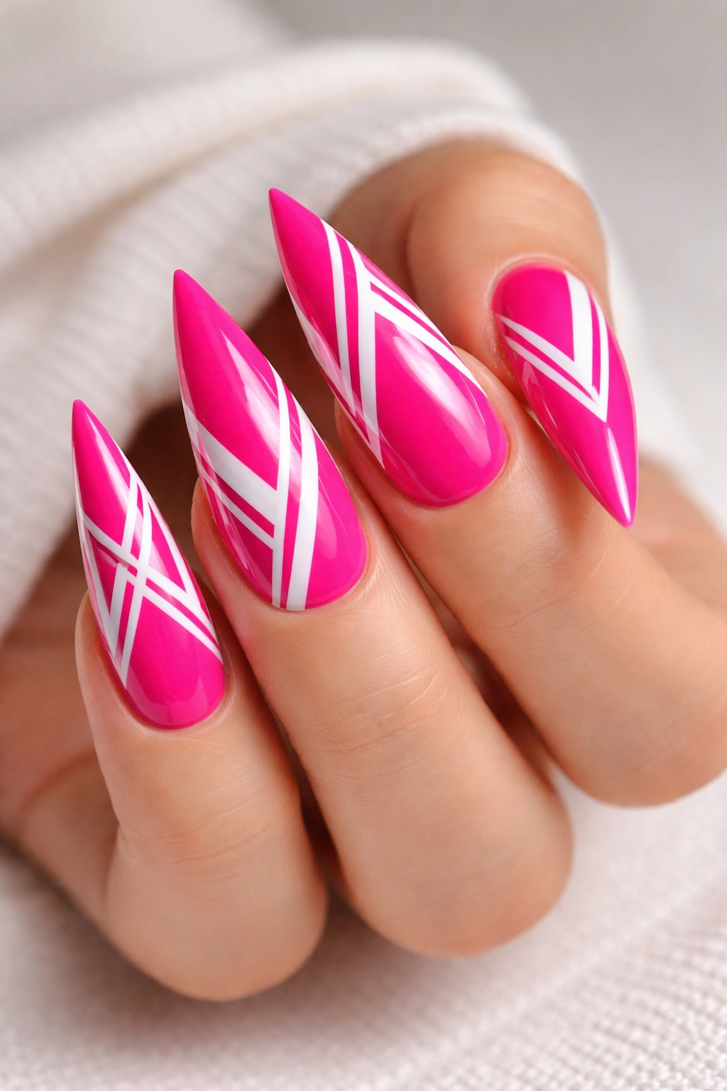 Close-up of hot pink stiletto nails with white geometric patterns on a neutral background