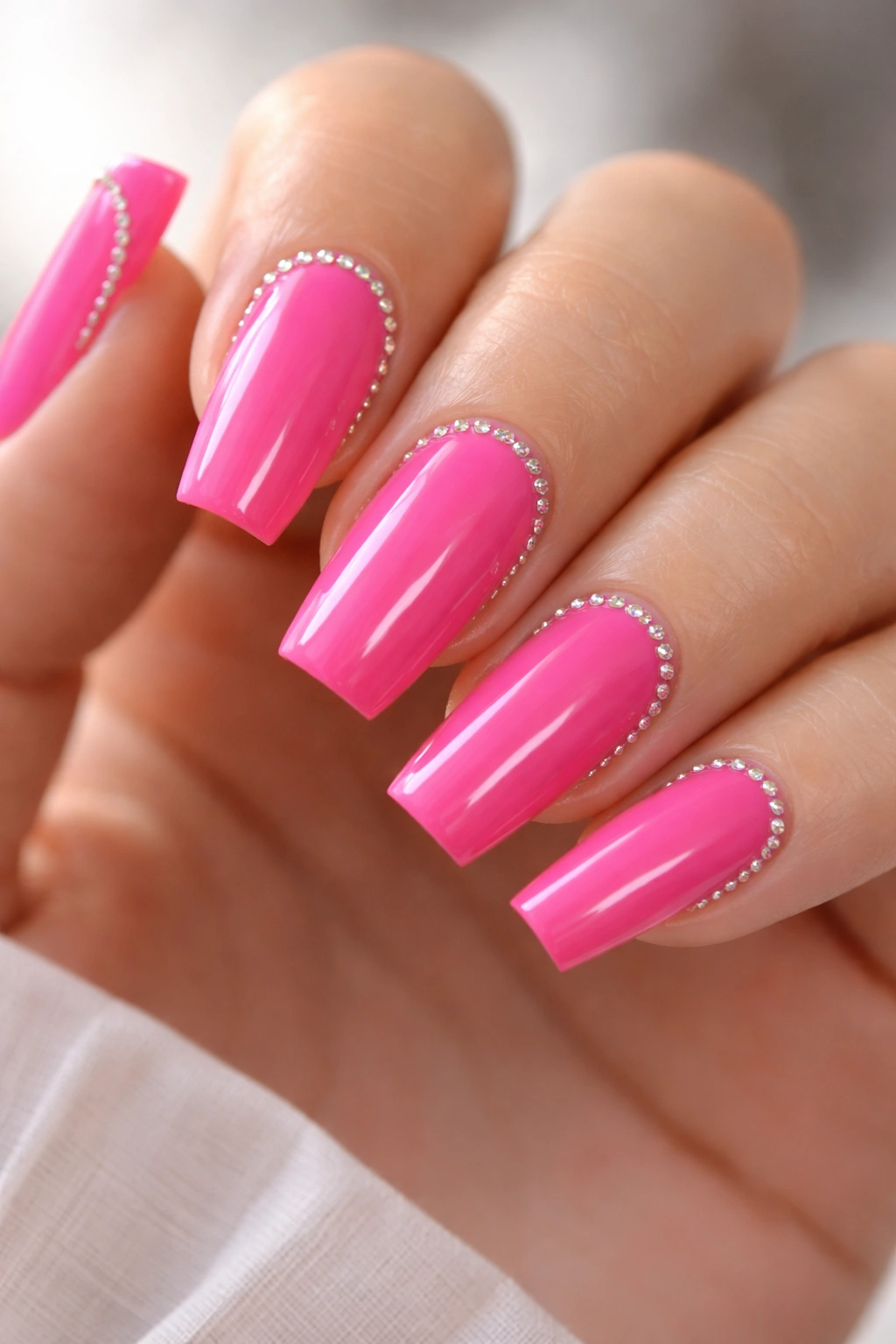 Close-up of hot pink coffin nails with micro-rhinestones along edges on medium-length nails