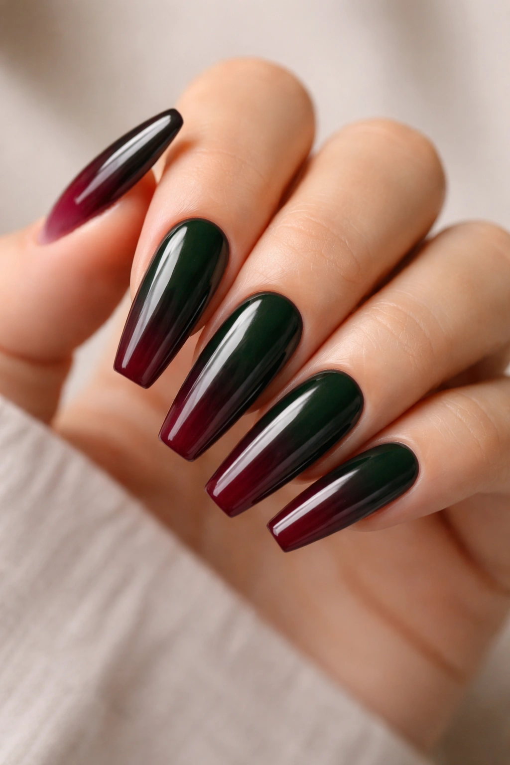 Close-up of hunter green to burgundy ombre coffin nails on a bare hand with glossy finish.