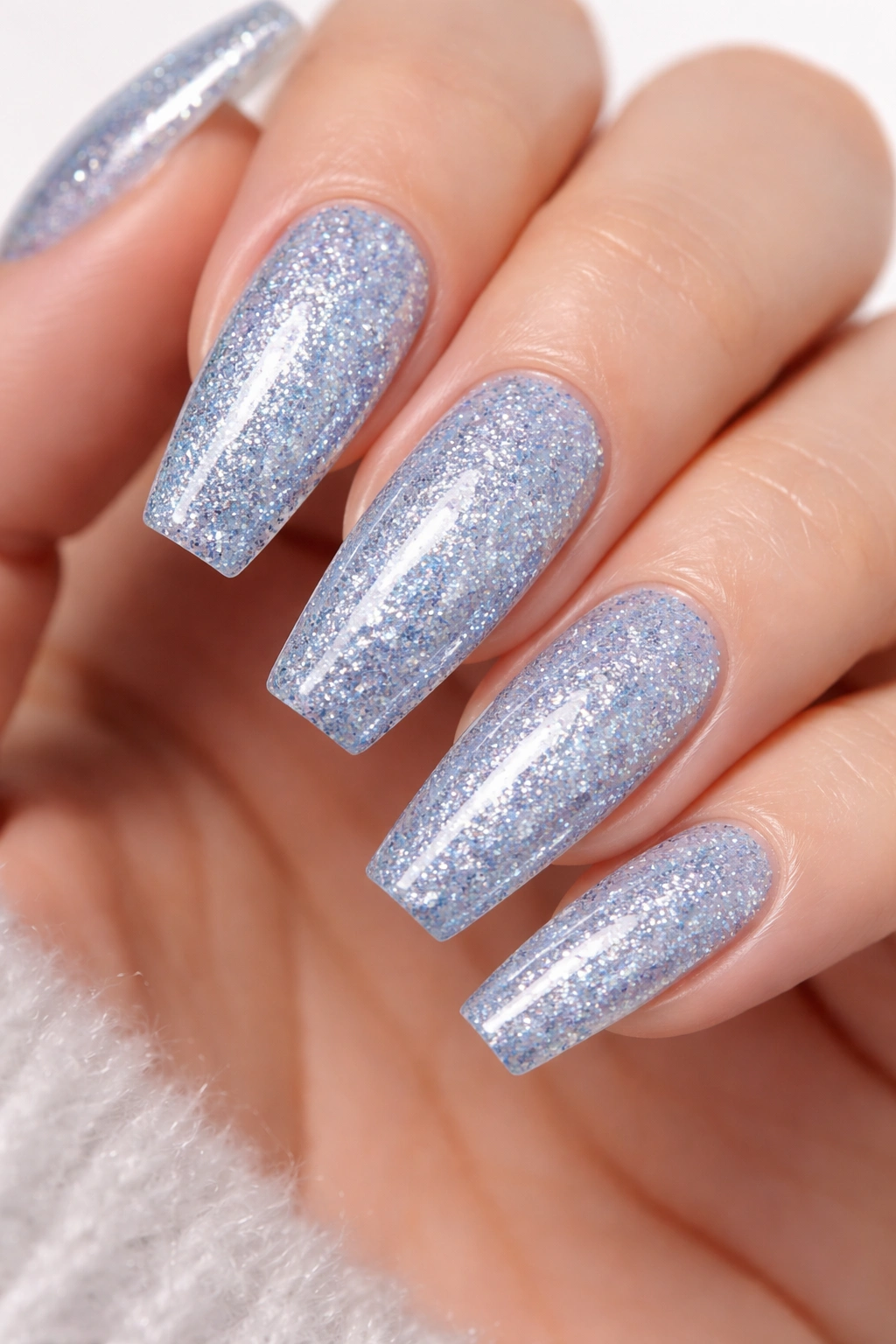 Close-up of nails with ice blue glitter in a clear base on medium coffin nails