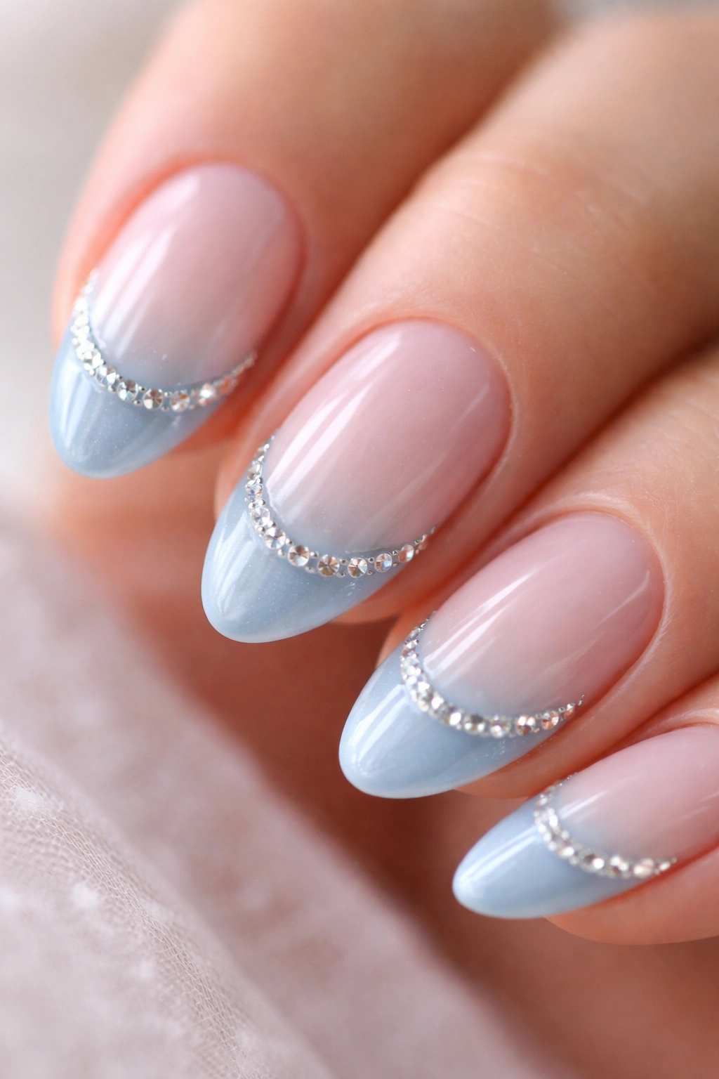 Close-up of a short almond nail with ice blue tip and crystal rhinestones along the boundary.