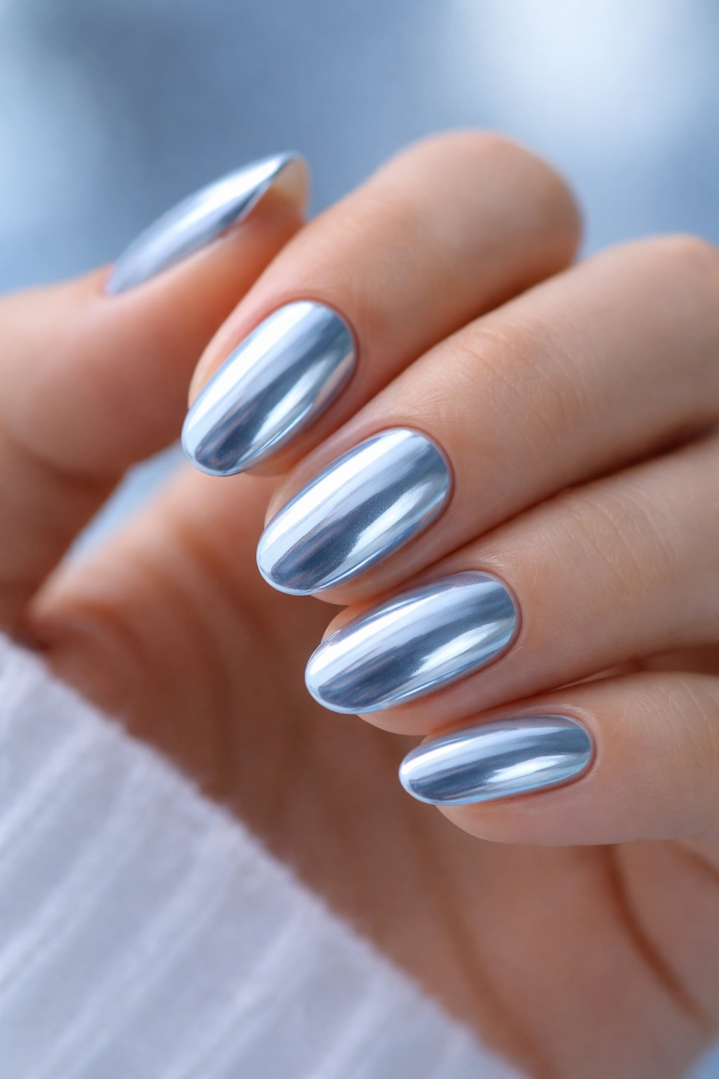 Close-up of short oval nails with icy blue chrome on pale blue base, cool reflection