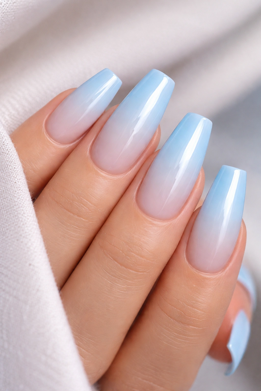 Close-up of icy blue gradient coffin nails on a neutral surface