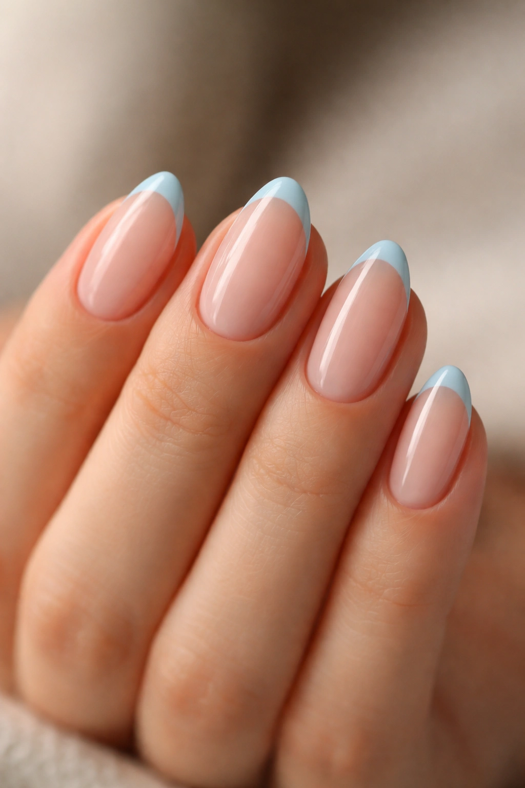 Close-up of short almond nails with icy blue micro French tips on a sheer pink-beige base