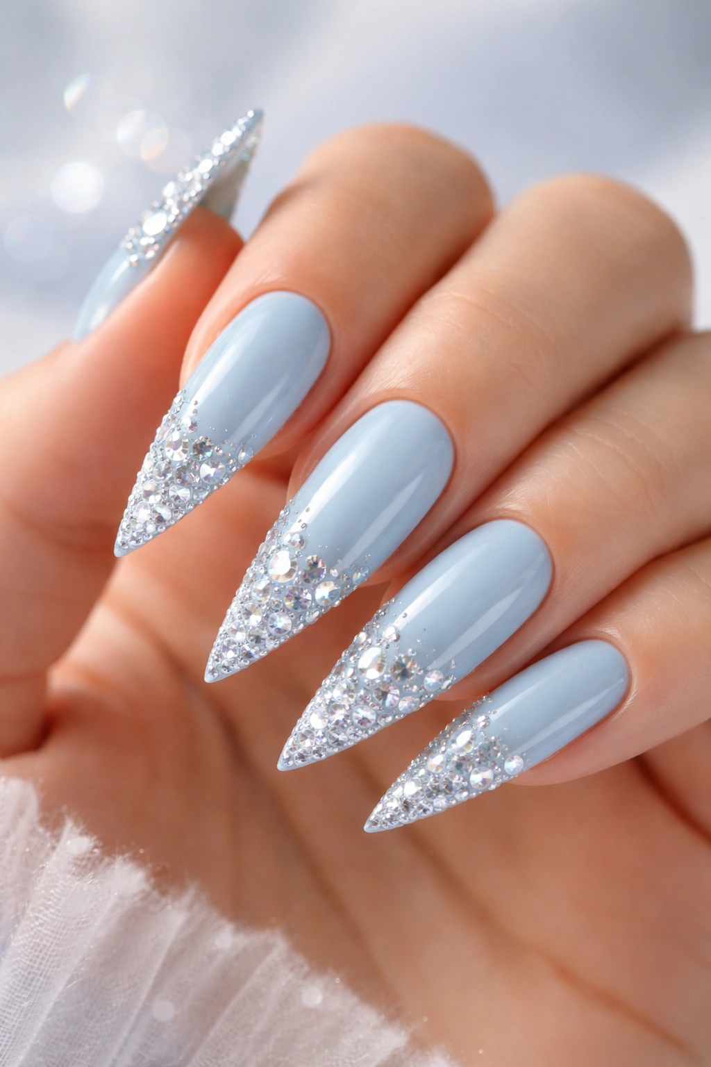 Close-up of icy blue stiletto nails with crystal encrusted tips on a hand