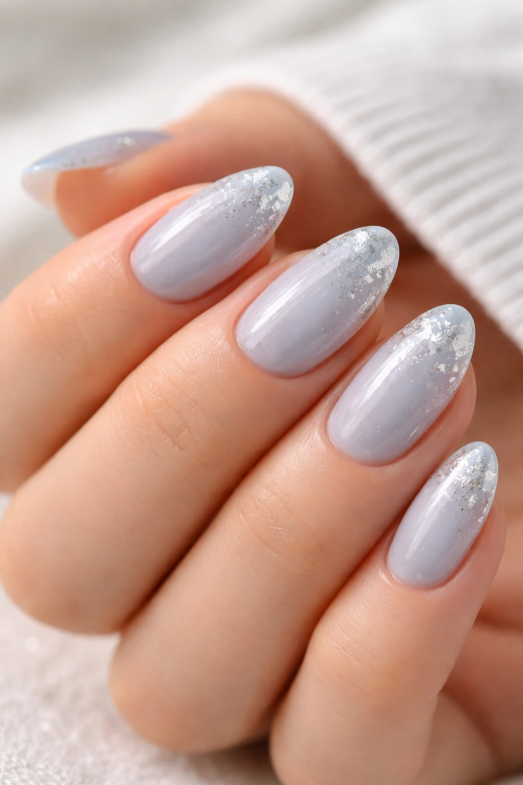 Short almond nails with icy blue polish and silver foil flecks near the tips