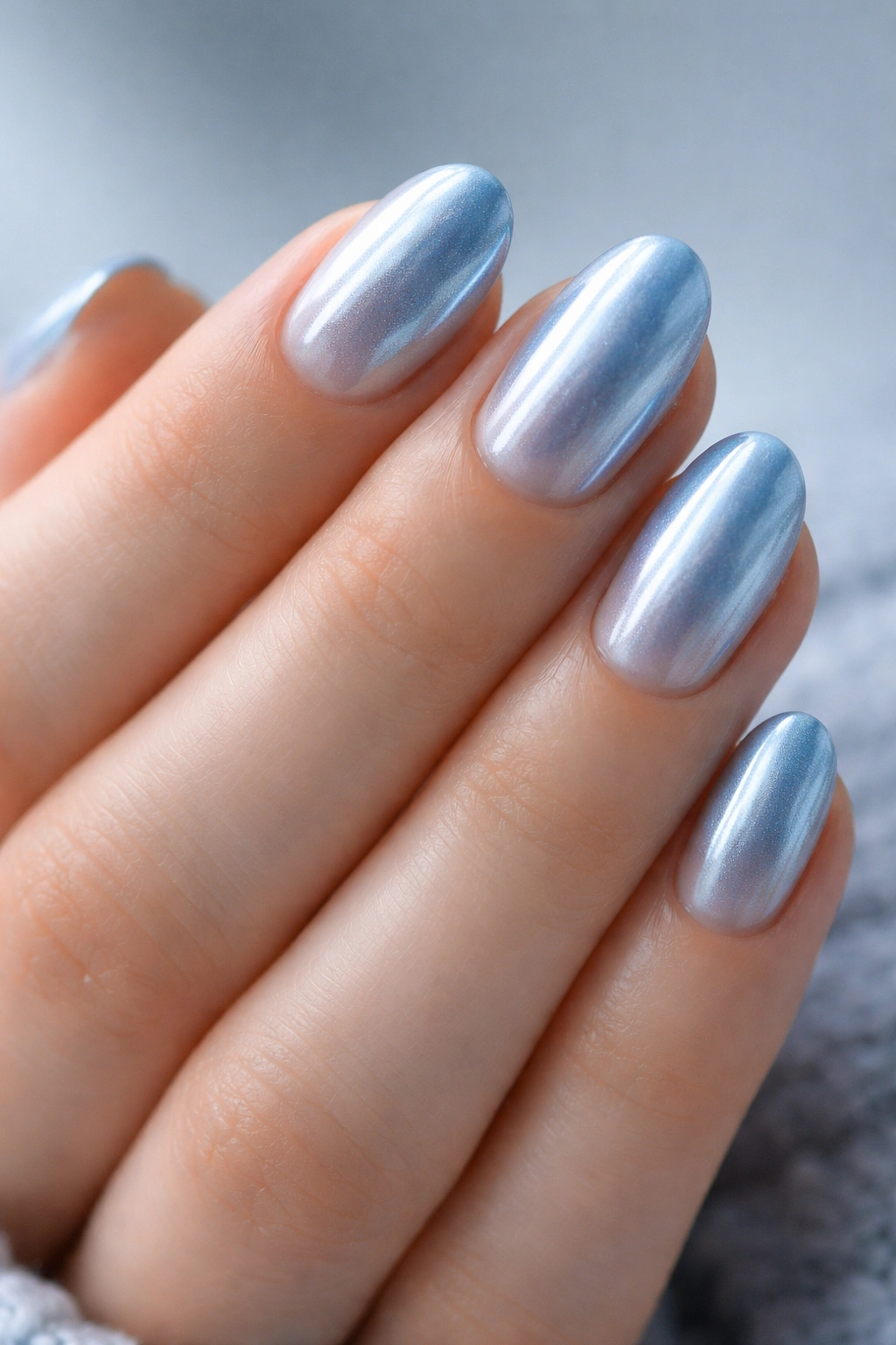 Close-up of icy chrome blue short oval nails with pale pink base, frosted metallic finish
