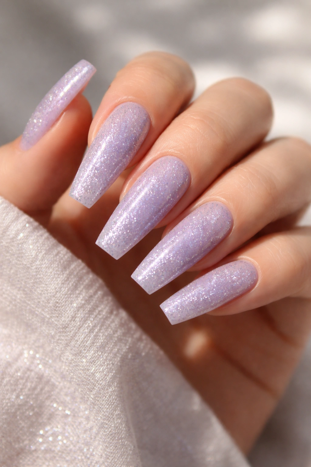 Icy lavender coffin nails with silver glitter sparkle on a pale hand