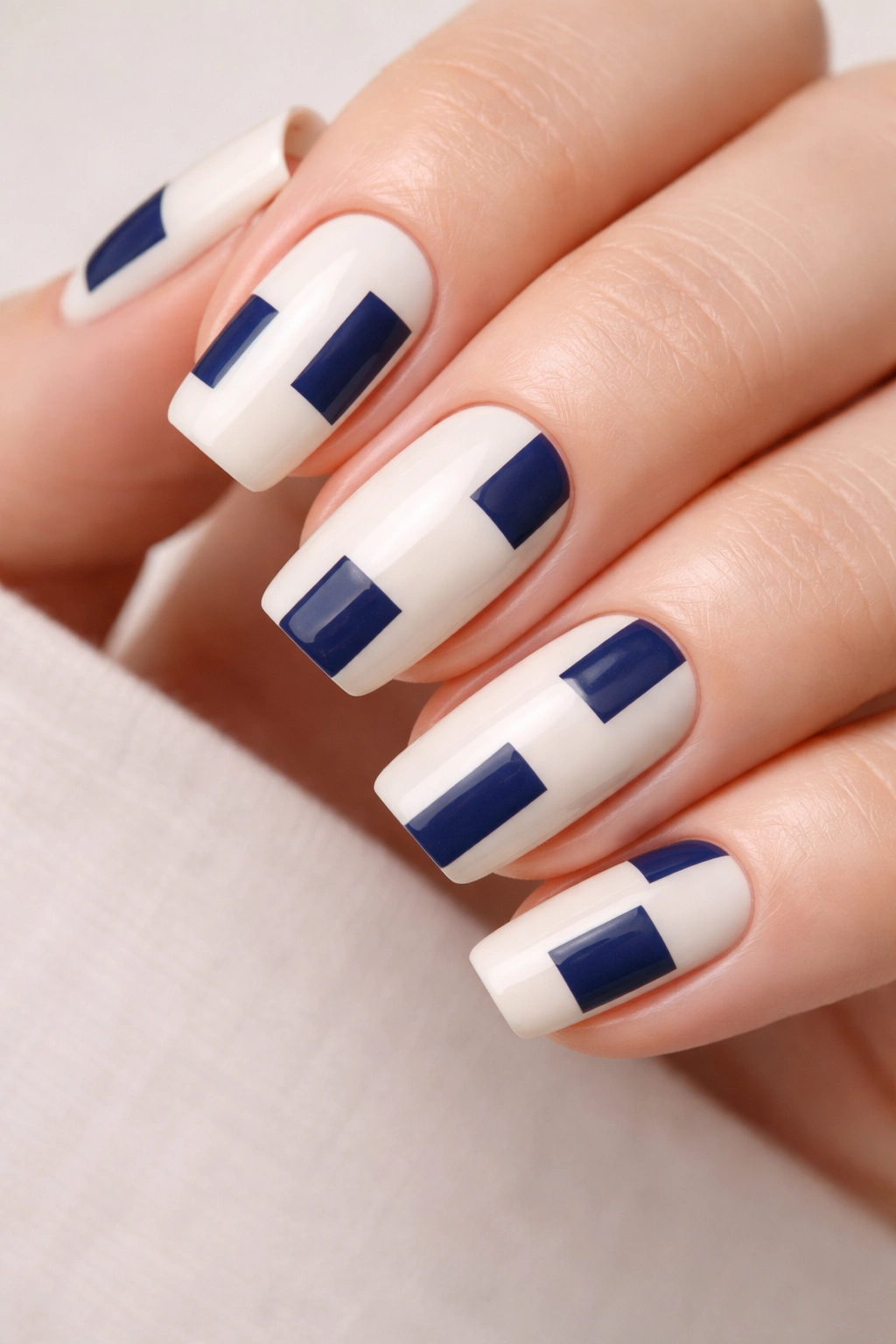 Close-up of ivory nails with navy geometric blocks on a neutral background